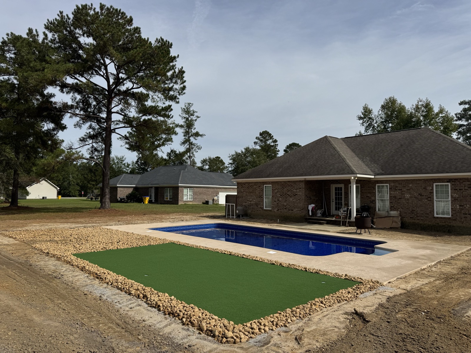 Custom putting green with river rock border beside a new 18x36 vinyl liner pool